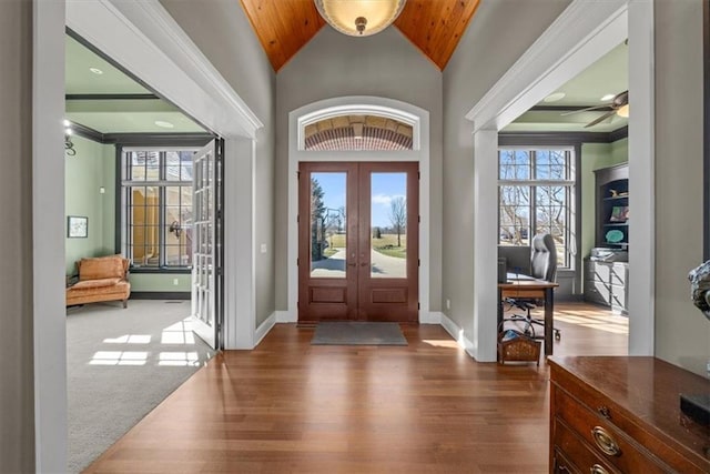 entrance foyer featuring crown molding, baseboards, lofted ceiling, french doors, and wood finished floors