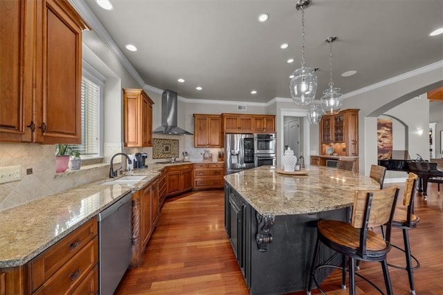 kitchen featuring arched walkways, a sink, stainless steel appliances, a large island, and wall chimney exhaust hood