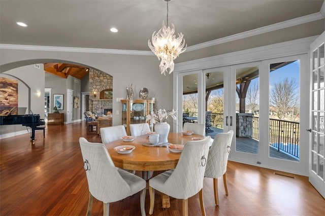 dining space with wood finished floors, a fireplace, crown molding, a chandelier, and vaulted ceiling