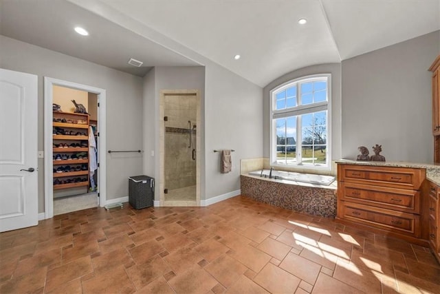 full bath with a walk in closet, baseboards, a garden tub, vaulted ceiling, and a stall shower