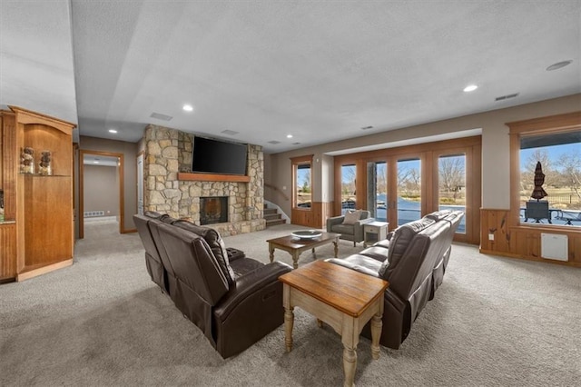 living room with a stone fireplace, light carpet, wainscoting, and a textured ceiling