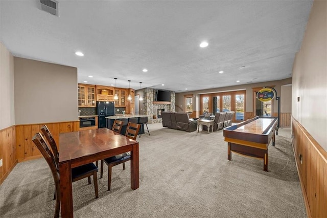 dining space with visible vents, light colored carpet, a stone fireplace, and wainscoting