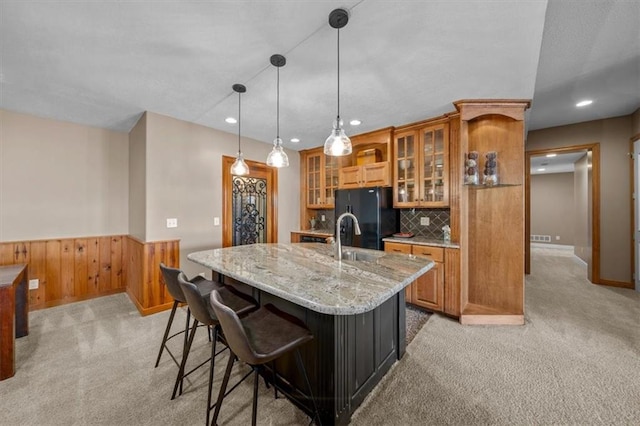 kitchen featuring light carpet, brown cabinets, wainscoting, and black fridge