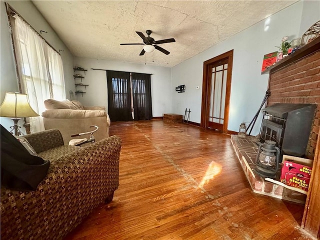 living room with ceiling fan, wood-type flooring, a textured ceiling, and a wood stove