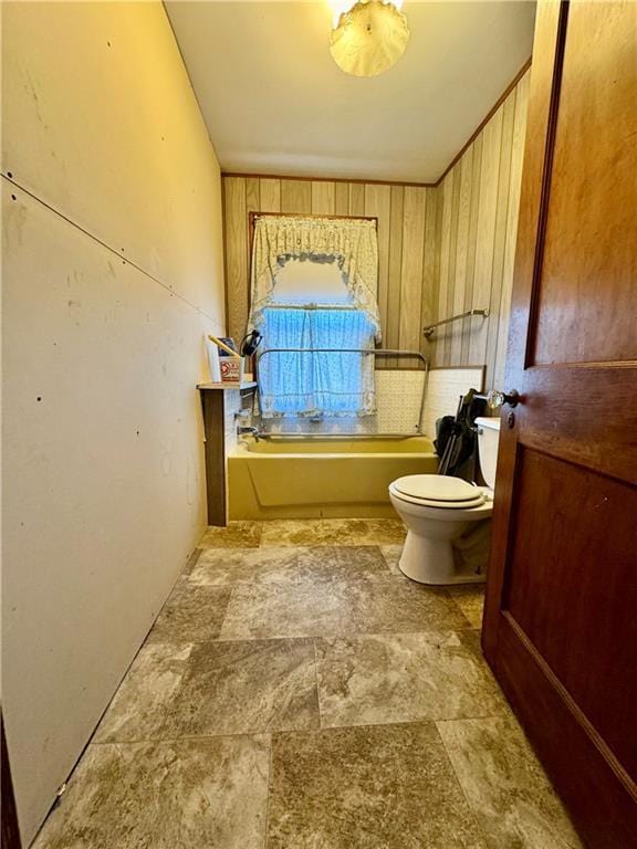 bathroom featuring a washtub, wooden walls, and toilet