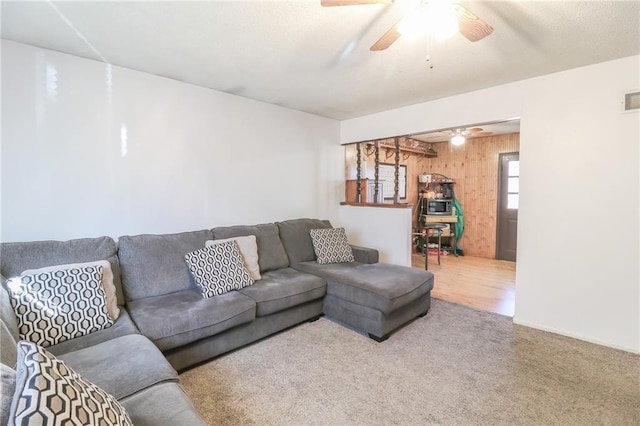 carpeted living room featuring wooden walls and ceiling fan