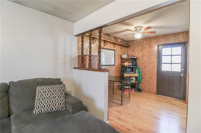 living room featuring ceiling fan, hardwood / wood-style floors, a textured ceiling, and wood walls