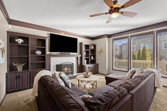 living room with carpet floors, a ceiling fan, baseboards, a tiled fireplace, and crown molding