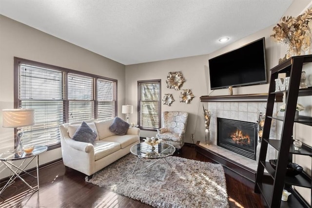 living area with a tile fireplace, a textured ceiling, baseboards, and wood finished floors