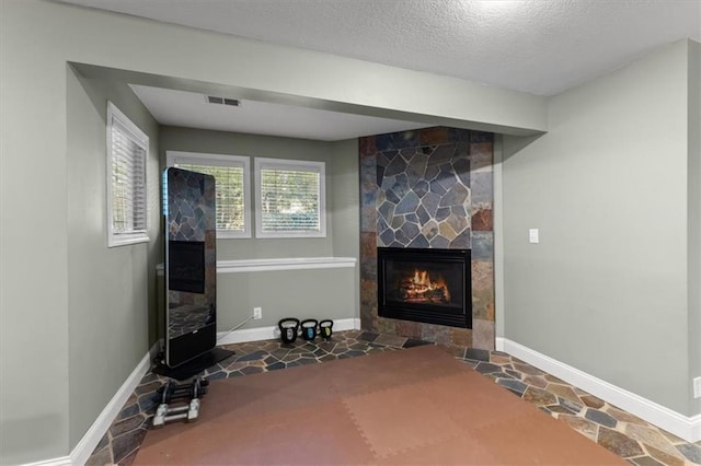 living area with baseboards, visible vents, a textured ceiling, and a stone fireplace