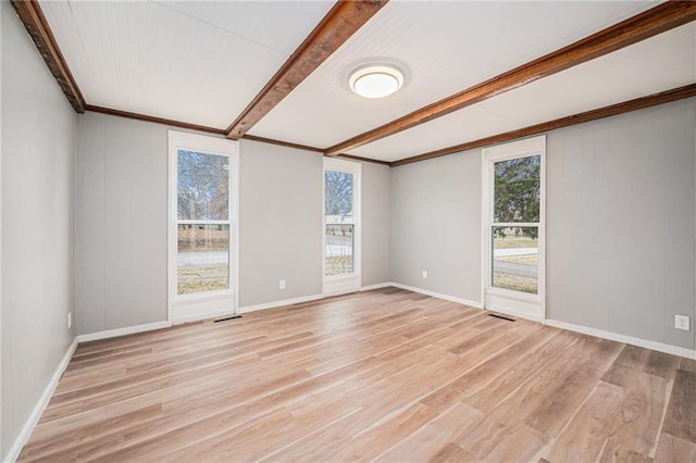 empty room with beamed ceiling, a healthy amount of sunlight, and light hardwood / wood-style floors