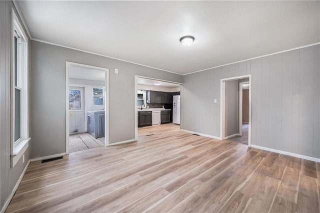 unfurnished living room featuring crown molding, sink, washing machine and clothes dryer, and light wood-type flooring