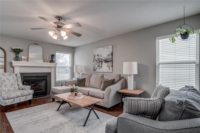 living room with a brick fireplace, a ceiling fan, and dark wood-type flooring