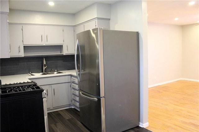 kitchen featuring sink, stainless steel refrigerator, hardwood / wood-style floors, gas stove, and decorative backsplash