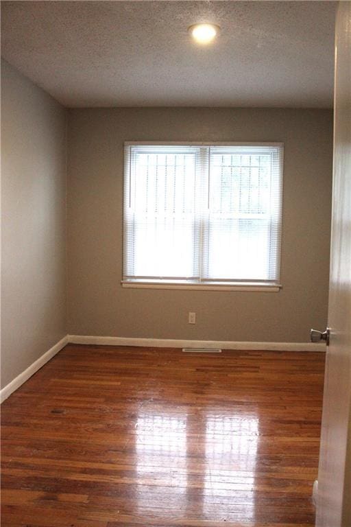 spare room featuring plenty of natural light, a textured ceiling, and dark hardwood / wood-style flooring