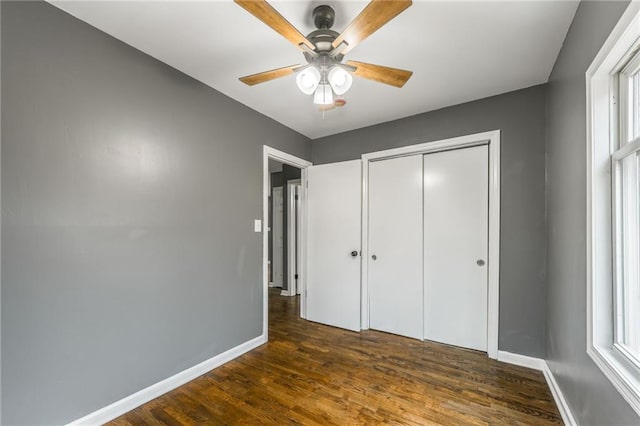 unfurnished bedroom with ceiling fan, a closet, dark hardwood / wood-style flooring, and multiple windows