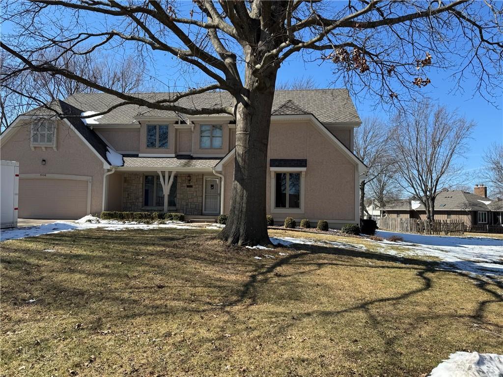 view of front of home with a garage, stone siding, a yard, and stucco siding