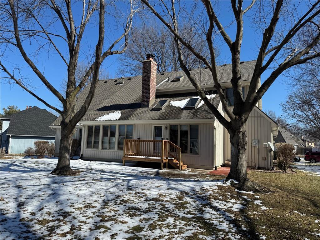 snow covered property with a shingled roof, a chimney, and a wooden deck