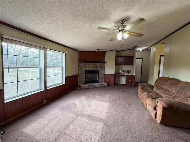 carpeted living room with a fireplace, wood walls, ornamental molding, ceiling fan, and a textured ceiling