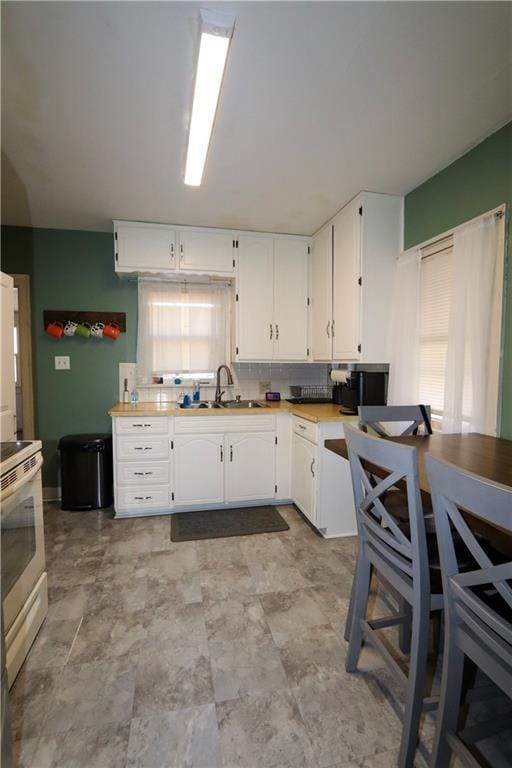 kitchen with tasteful backsplash, white electric stove, sink, and white cabinets