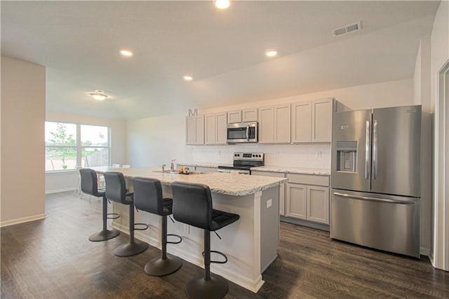 kitchen with a breakfast bar area, appliances with stainless steel finishes, dark hardwood / wood-style flooring, an island with sink, and backsplash