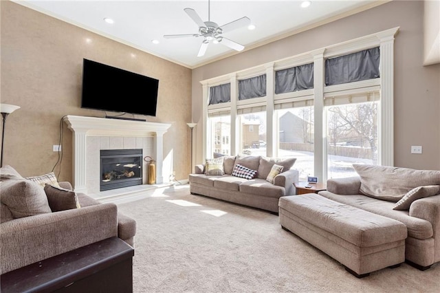 carpeted living room with a tiled fireplace, crown molding, and ceiling fan