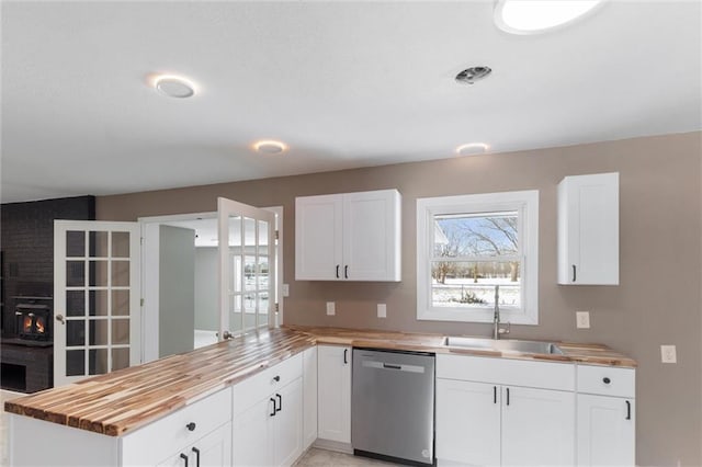 kitchen featuring stainless steel dishwasher, wooden counters, sink, and white cabinets