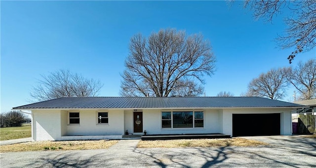 ranch-style home featuring brick siding, a garage, driveway, and metal roof