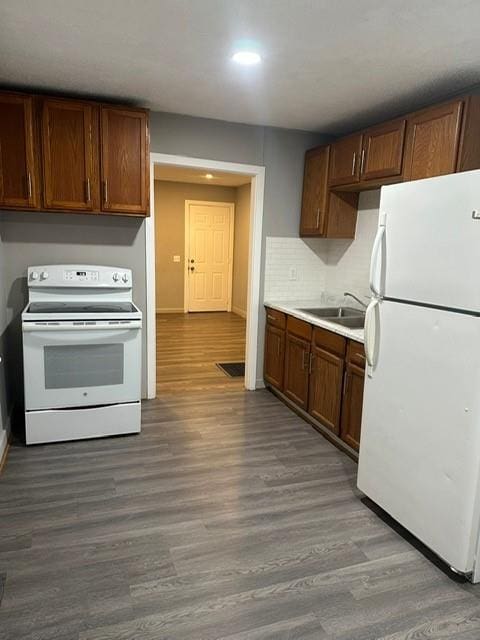 kitchen with dark wood-type flooring, white appliances, sink, and decorative backsplash