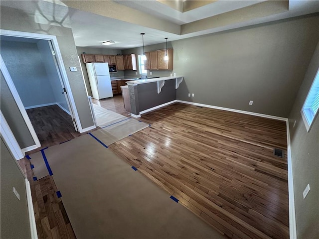 kitchen featuring pendant lighting, white refrigerator, a kitchen bar, dark hardwood / wood-style flooring, and kitchen peninsula