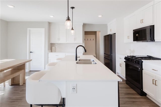 kitchen featuring white cabinets, a sink, black appliances, wood finished floors, and a kitchen breakfast bar