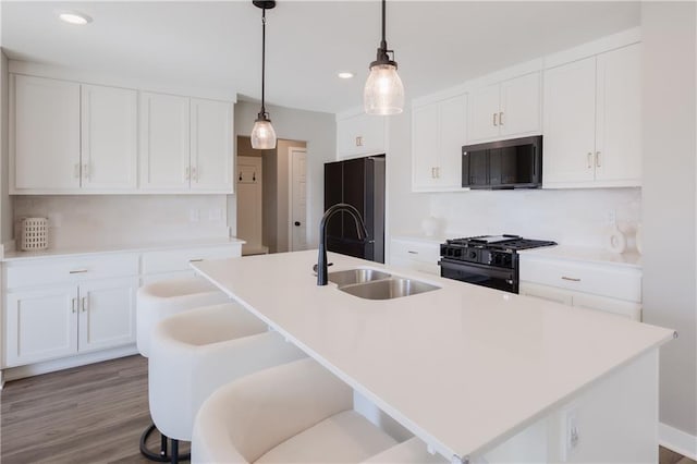 kitchen featuring hanging light fixtures, a kitchen island with sink, a sink, white cabinetry, and black appliances