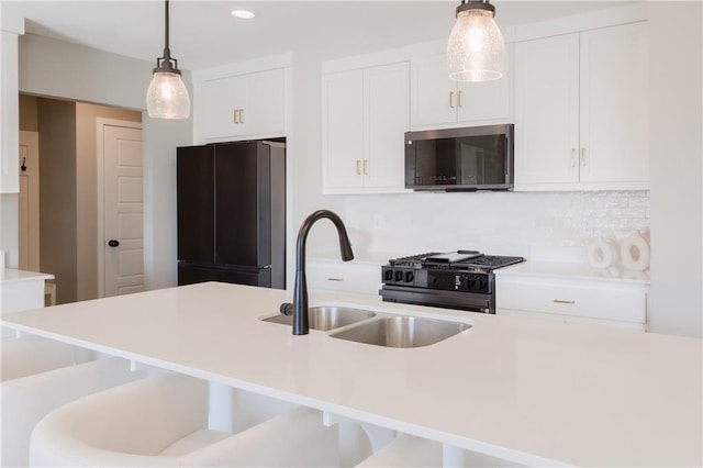 kitchen with black appliances, a sink, white cabinets, and pendant lighting