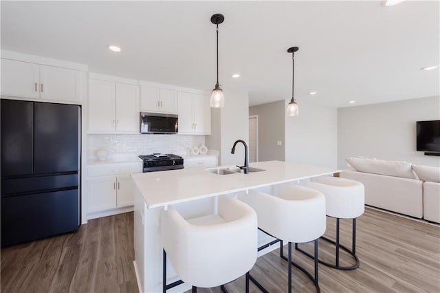 kitchen featuring white cabinets, stove, stainless steel microwave, freestanding refrigerator, and a sink