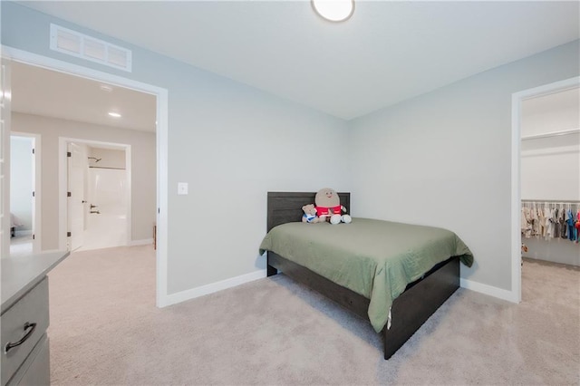 bedroom with light colored carpet, visible vents, baseboards, and a spacious closet