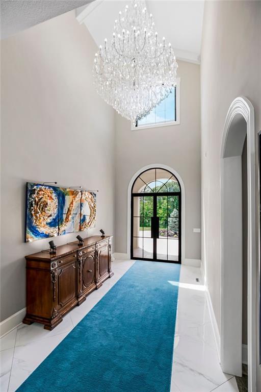 entryway featuring high vaulted ceiling, a notable chandelier, baseboards, marble finish floor, and french doors