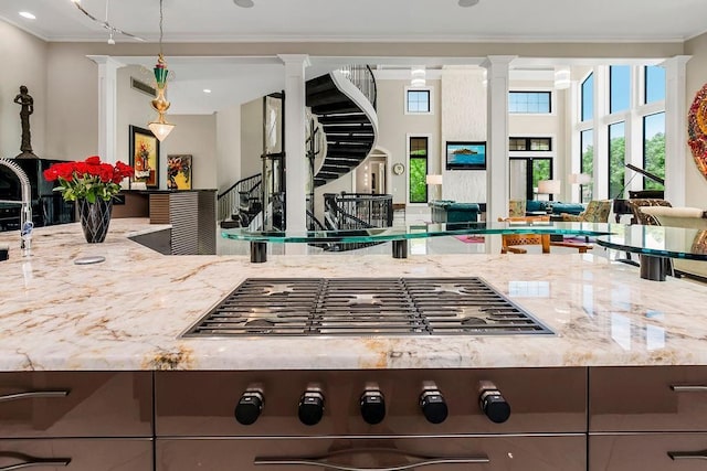 kitchen featuring ornate columns, light stone counters, open floor plan, and crown molding