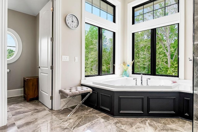 bathroom featuring plenty of natural light, a garden tub, and baseboards