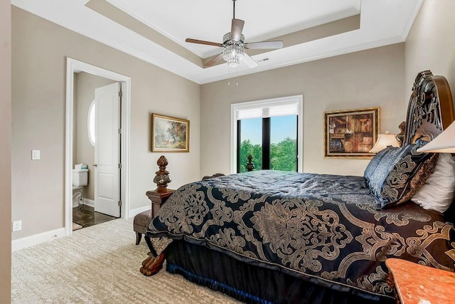 bedroom with a ceiling fan, baseboards, ornamental molding, a raised ceiling, and ensuite bath