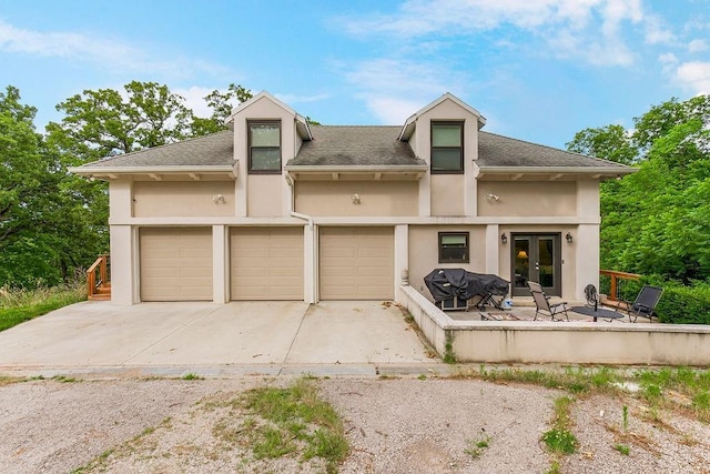 view of front of house with an attached garage, concrete driveway, french doors, roof with shingles, and stucco siding