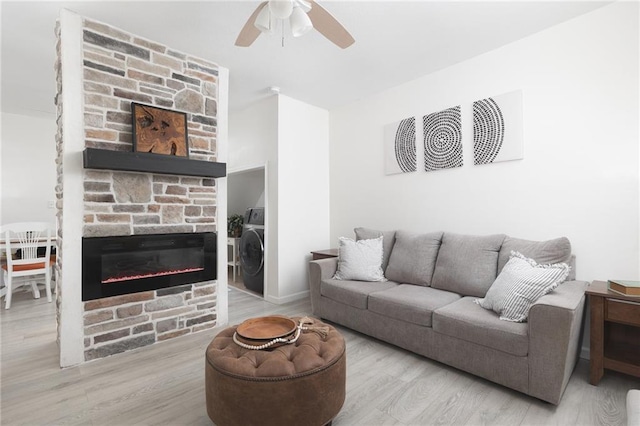 living room featuring ceiling fan, a stone fireplace, washer / dryer, and light hardwood / wood-style floors