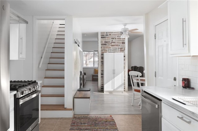 kitchen featuring light tile patterned floors, appliances with stainless steel finishes, white cabinets, ceiling fan, and backsplash