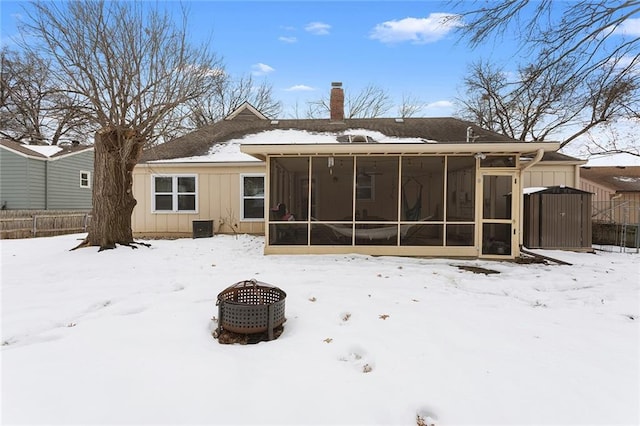 snow covered rear of property with a sunroom and an outdoor fire pit