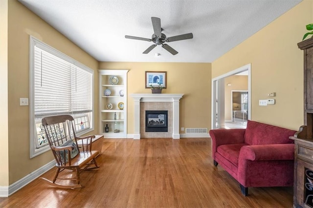 living area with visible vents, wood finished floors, ceiling fan, and a tile fireplace