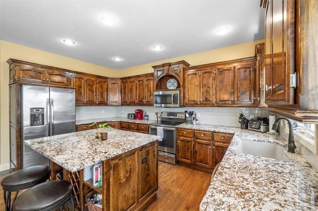 kitchen featuring a kitchen island, light wood-style flooring, a kitchen breakfast bar, stainless steel appliances, and a sink