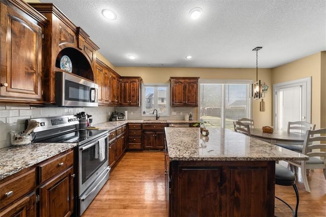 kitchen featuring a center island, light stone countertops, light wood-type flooring, a kitchen bar, and stainless steel appliances