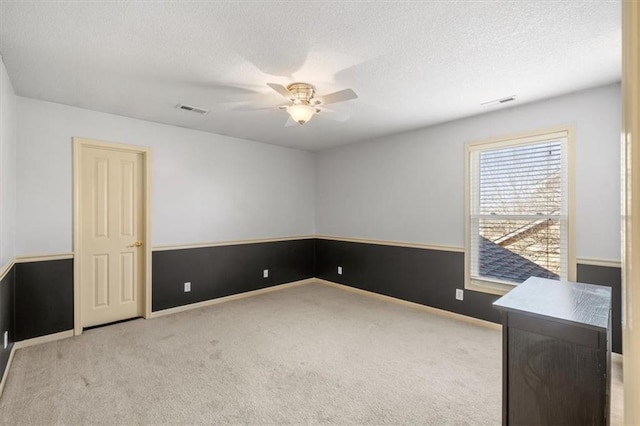 spare room with visible vents, a textured ceiling, carpet flooring, and a ceiling fan