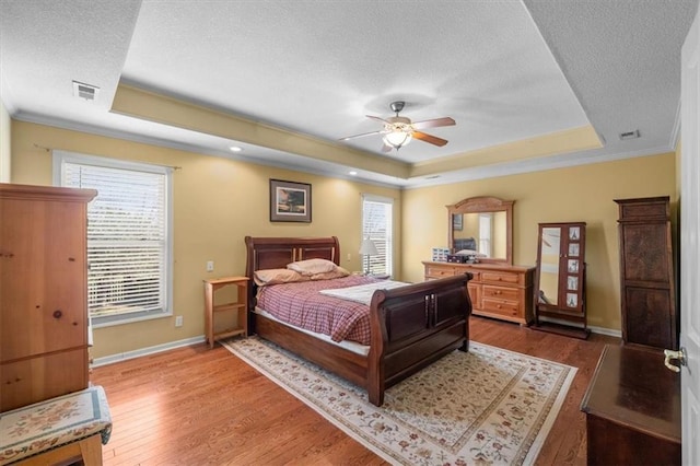 bedroom with visible vents, a textured ceiling, a tray ceiling, and wood finished floors