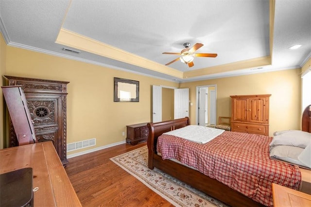 bedroom with wood finished floors, visible vents, baseboards, a tray ceiling, and ornamental molding