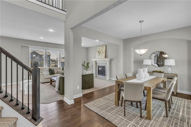 dining area with baseboards, dark wood finished floors, a glass covered fireplace, stairs, and recessed lighting